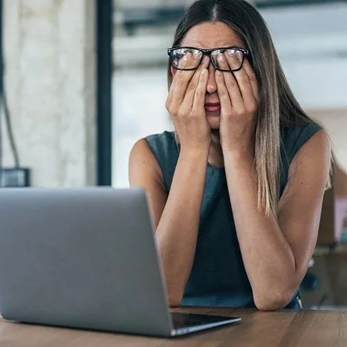 Woman sitting in front of computer rubbing her eyes in distress