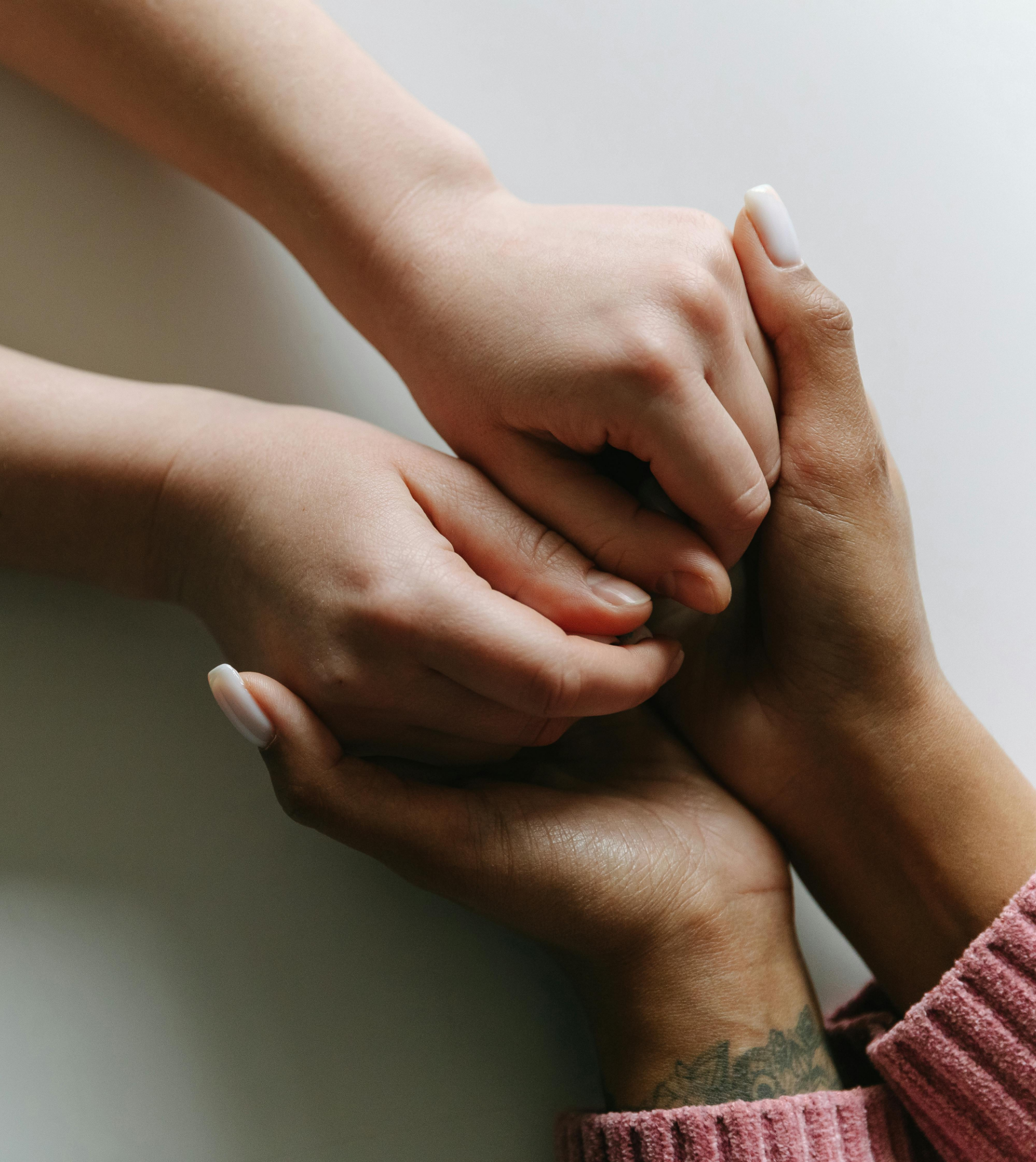 Close-up of one person holding hands with another person, with visible arm tattoos and a pink textured sleeve.