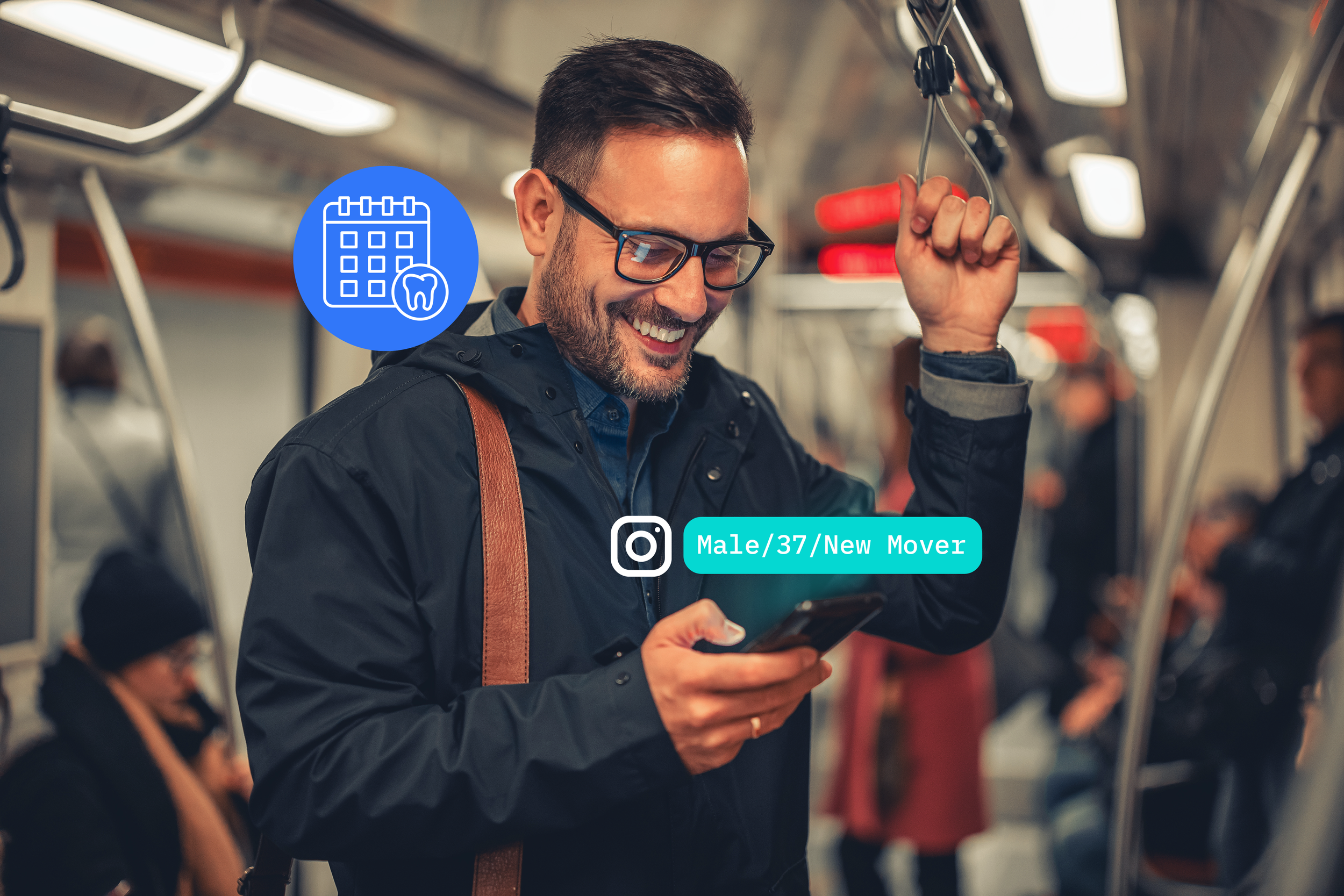 A man with dark hair, glasses, and a beard, smiling while looking at his phone, in a subway train. He is wearing a dark jacket with a brown strap over his shoulder. There are other passengers in the background.