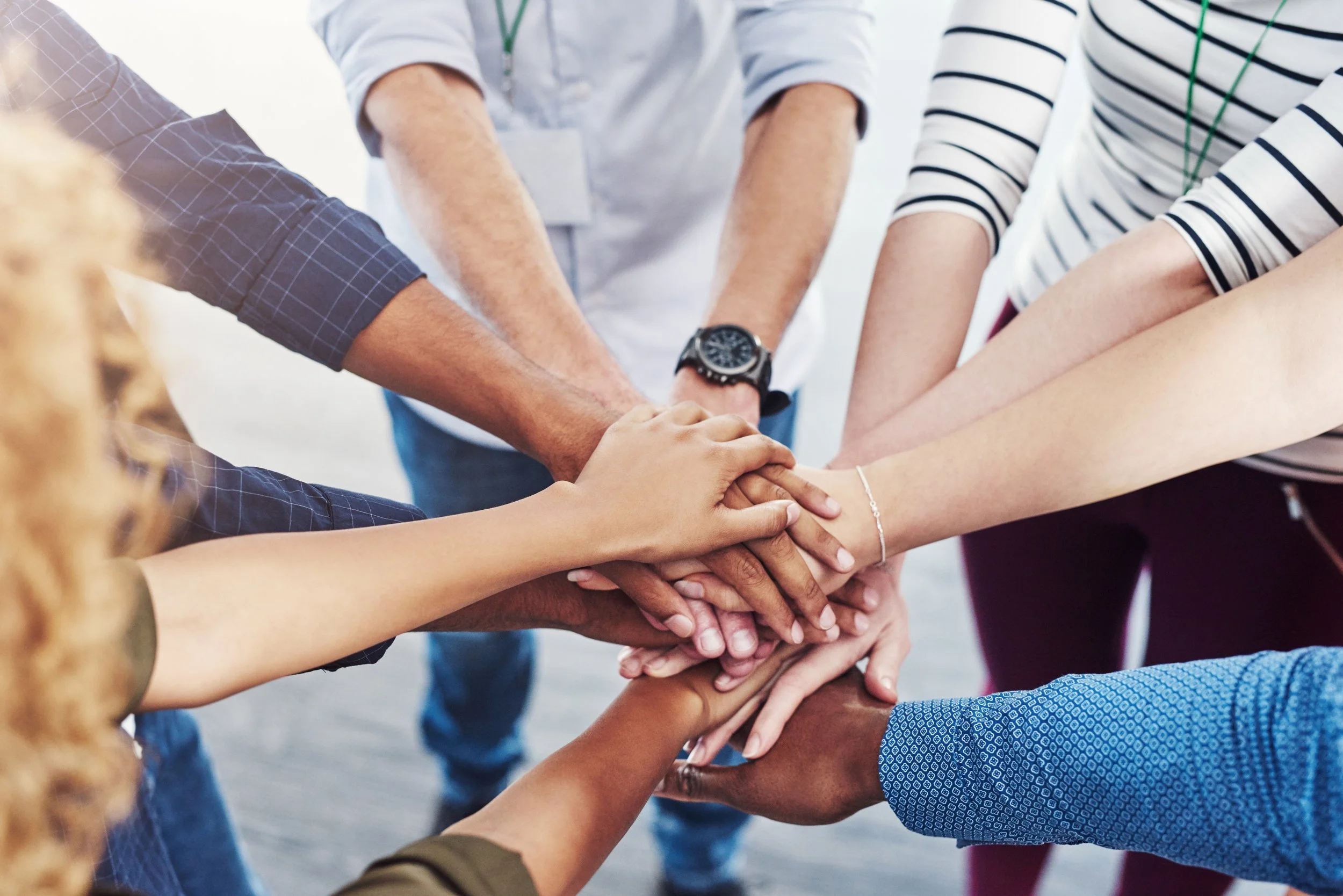 People of diverse backgrounds with their hands stacked together in a show of unity and teamwork.