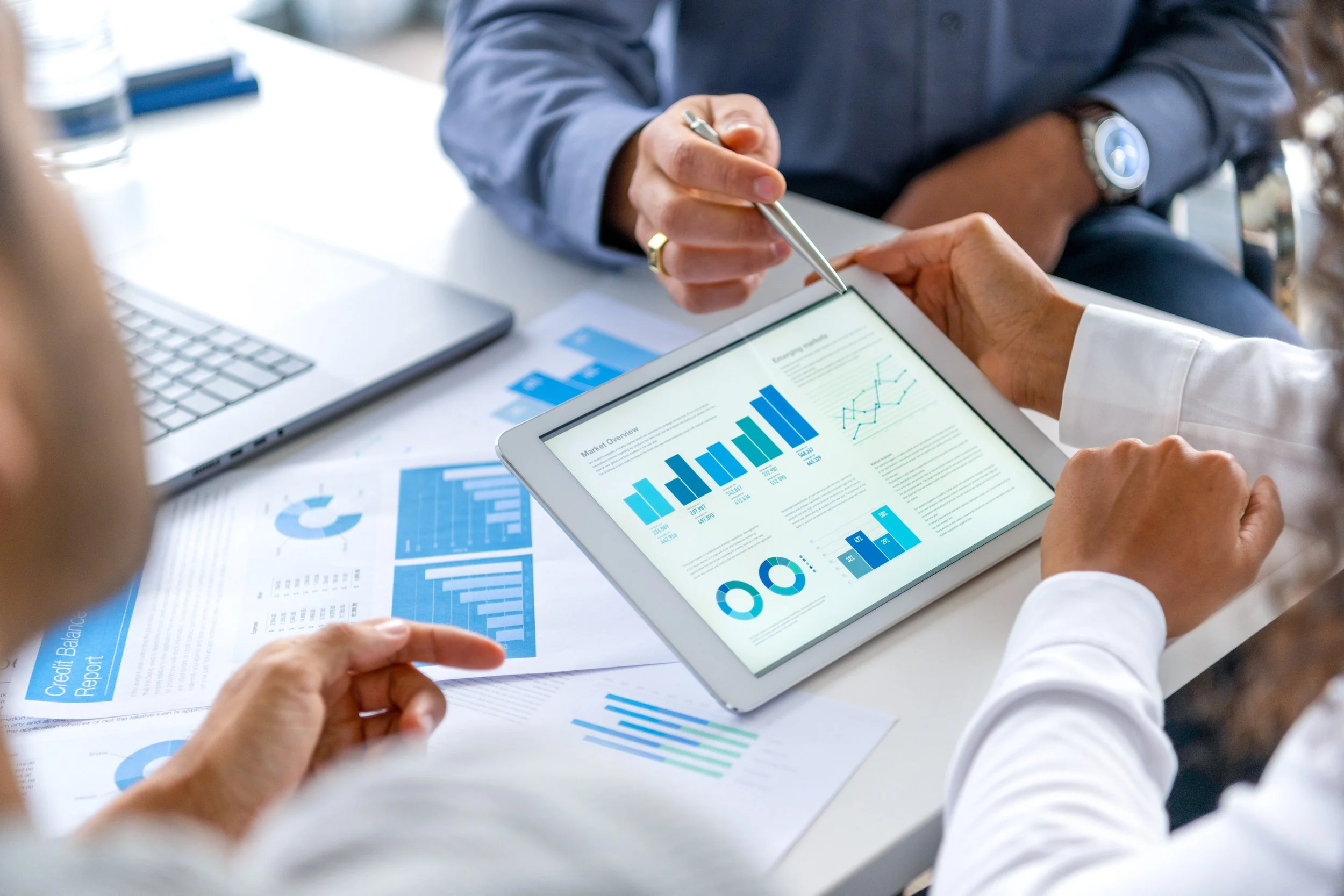 Business professionals in a meeting reviewing data charts and graphs on a tablet and printed reports.