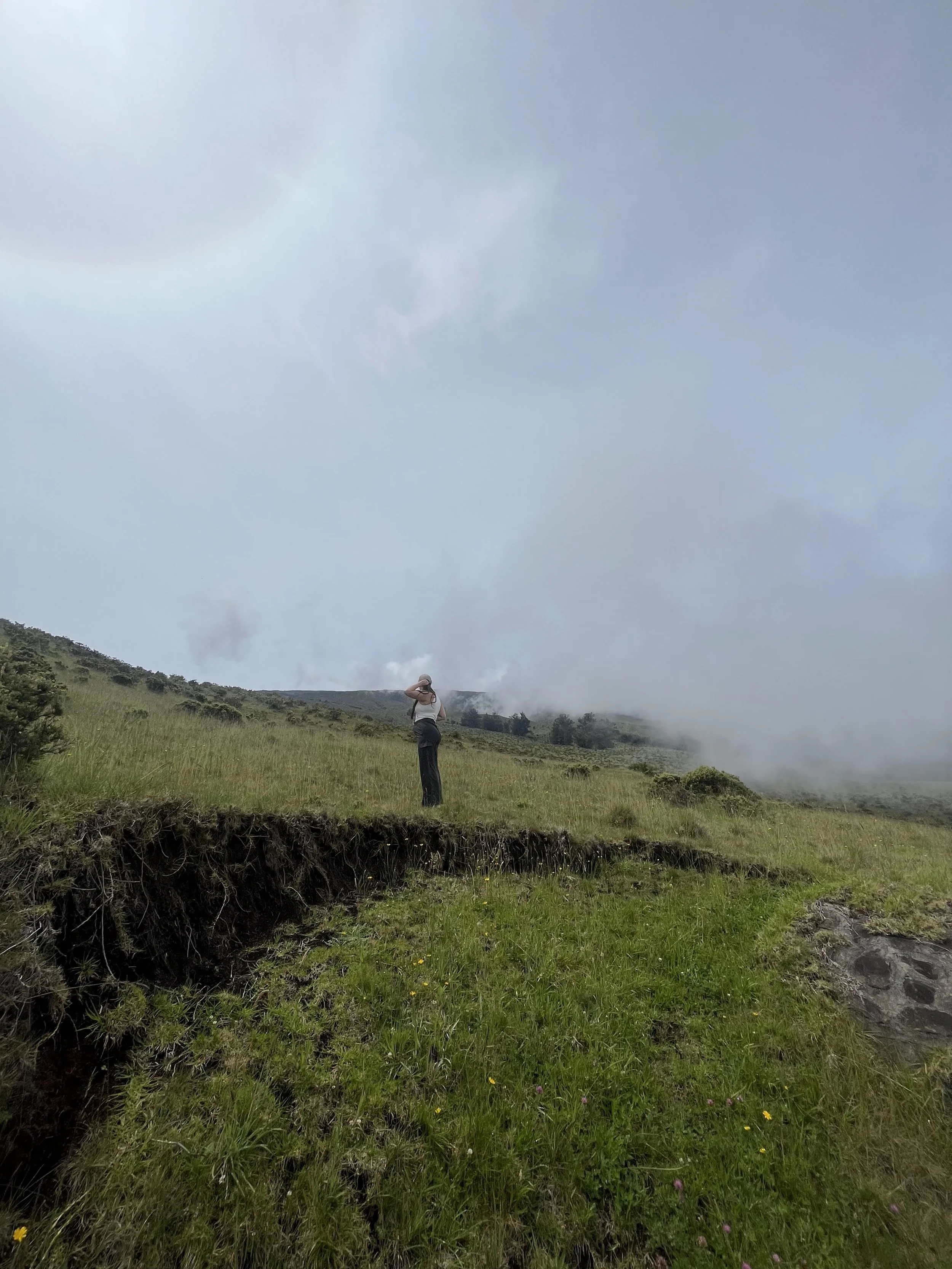 R Photos photographer Rachel Kosky exploring a dramatic misty volcanic hillside, green grass and rolling fog stretching to the horizon — available for destination elopements and adventure sessions worldwide