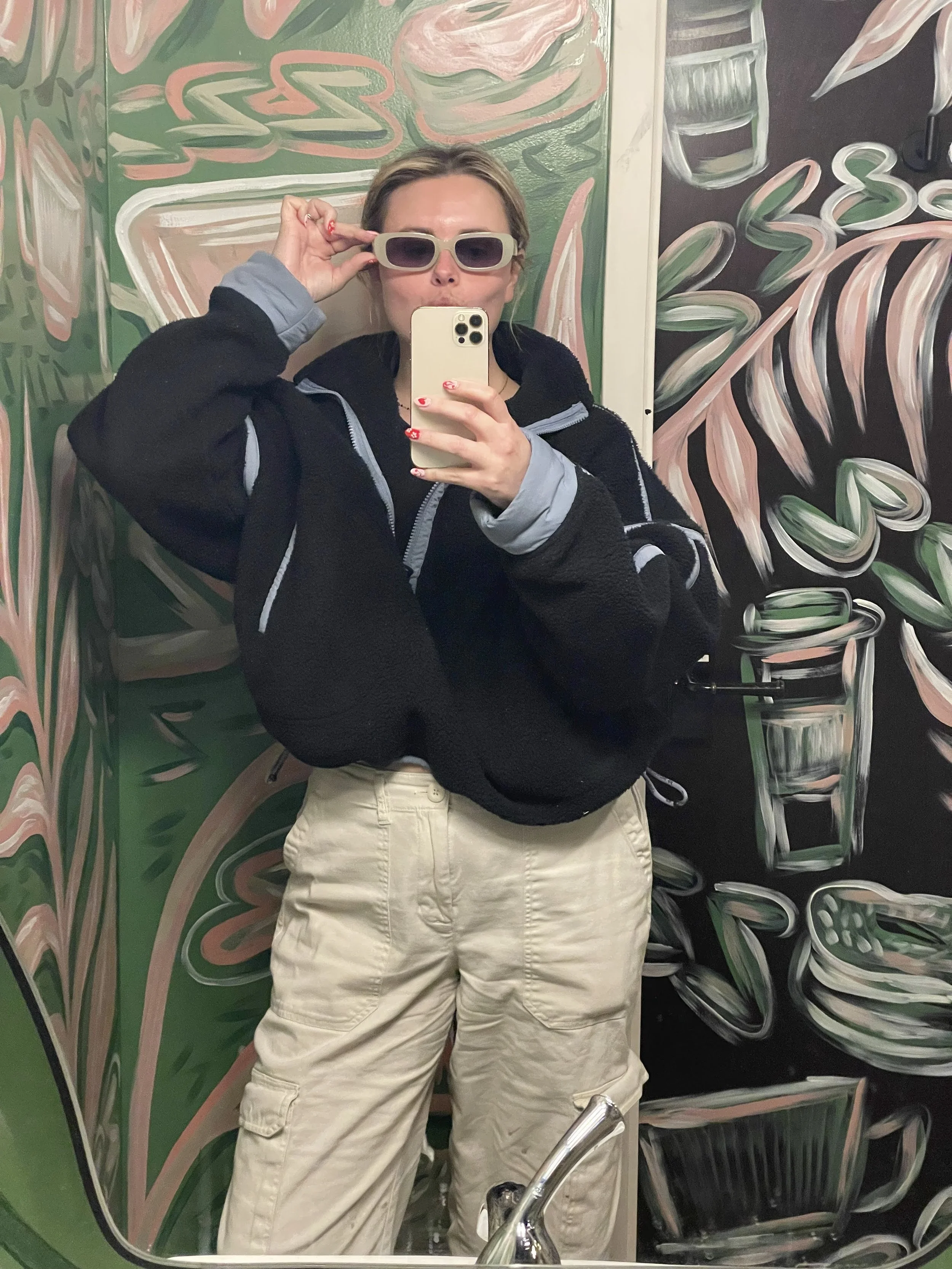 Candid mirror selfie of a blonde woman in sunglasses and a black fleece jacket in a colorful mural bathroom — Tennessee wedding photographer with personality