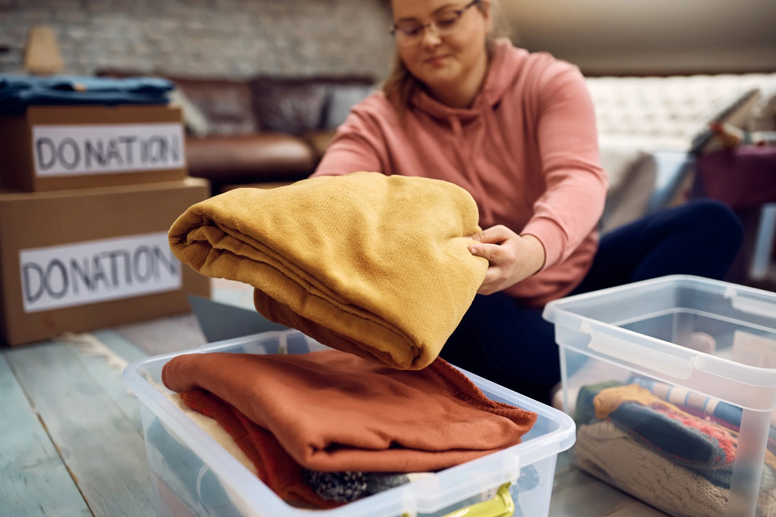 A woman organizing folded clothes on a table at a donation center with donation boxes in the background.