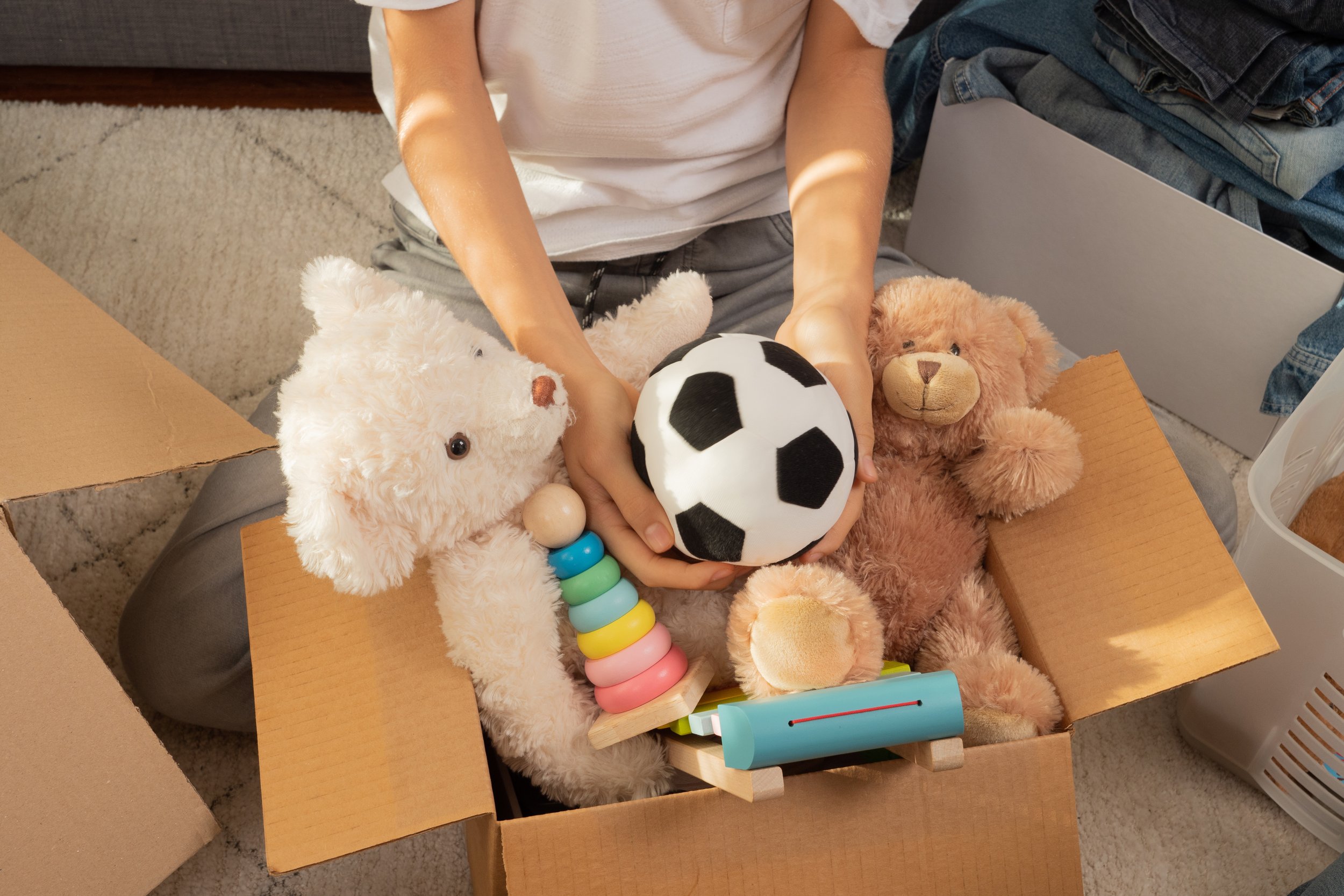 Person packing a box with stuffed animals, a toy soccer ball, and various toys inside.