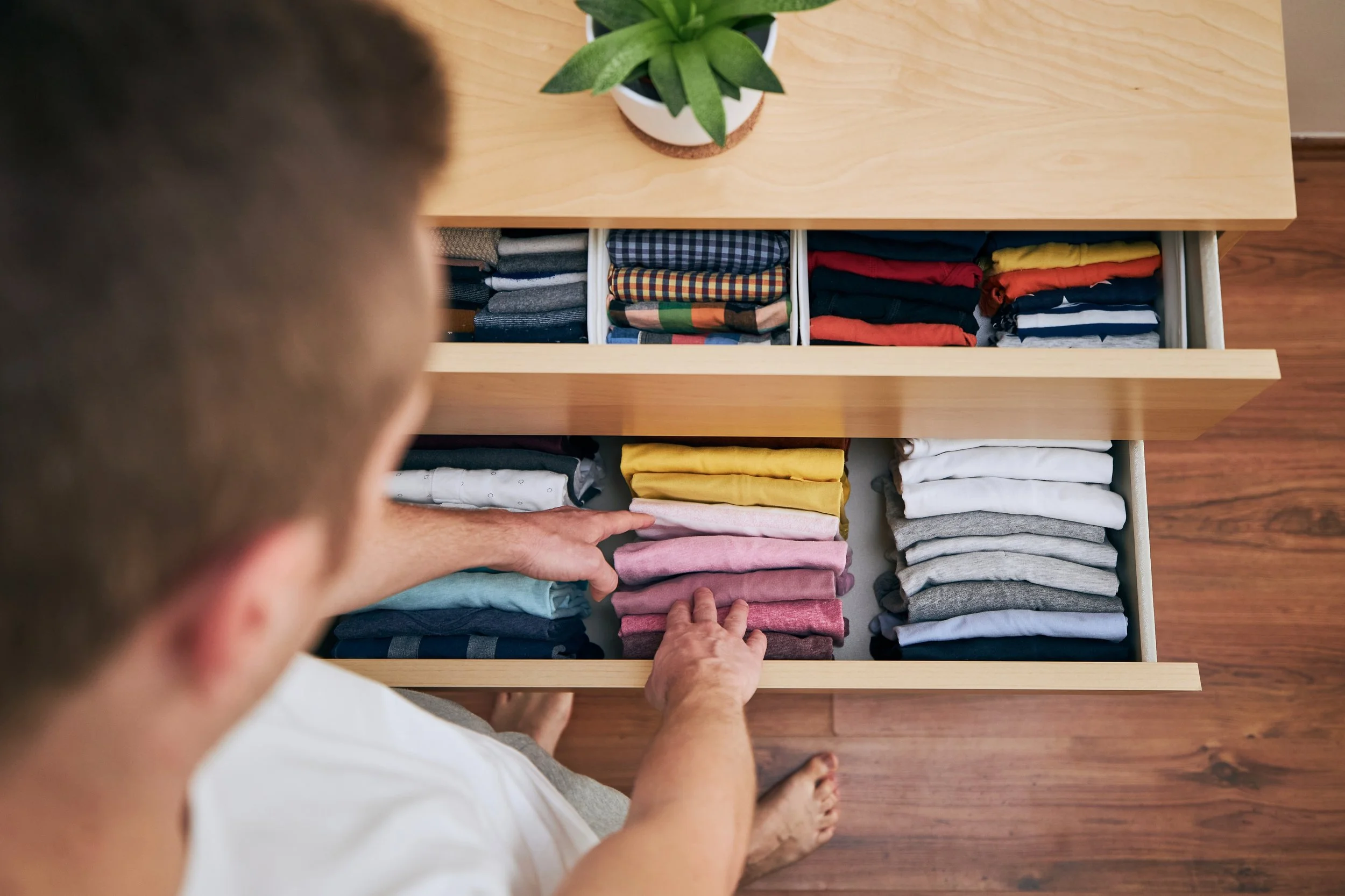 Person folding clothes in a drawer filled with neatly folded shirts of various colors.