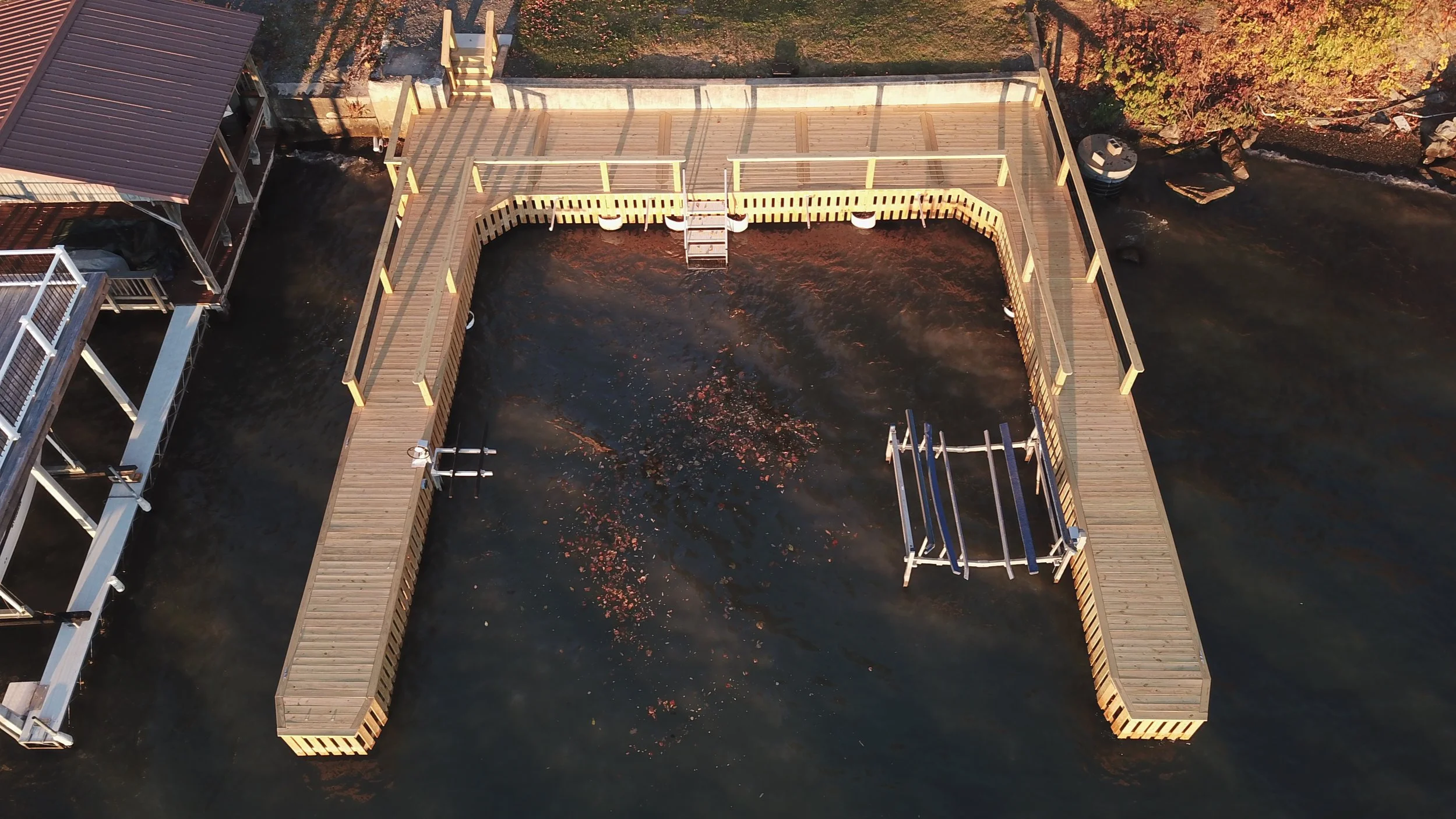 Aerial view of a wooden dock with railings over a body of water, surrounded by trees with autumn foliage.