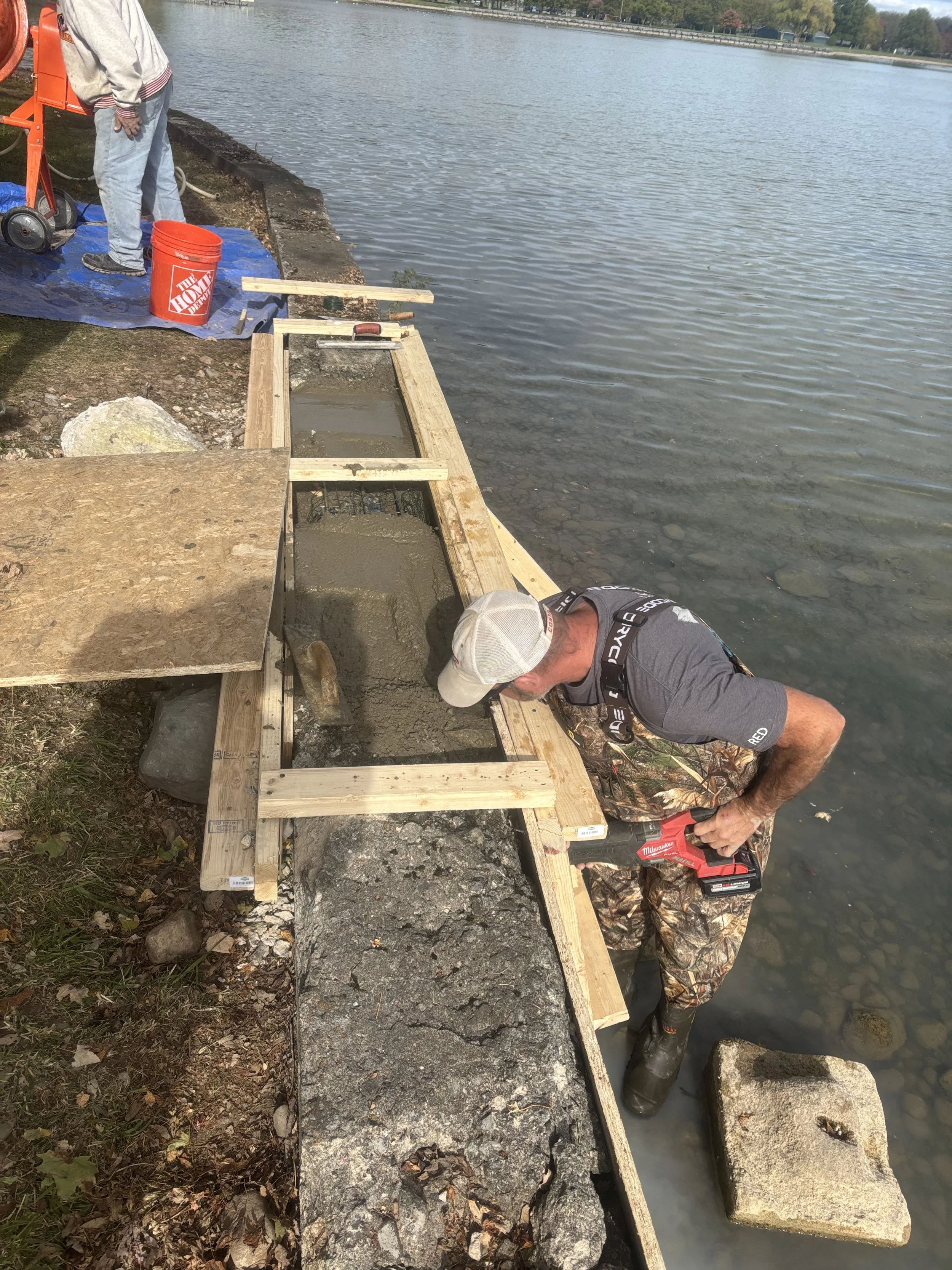 Workers building a wooden frame near a body of water using power tools.