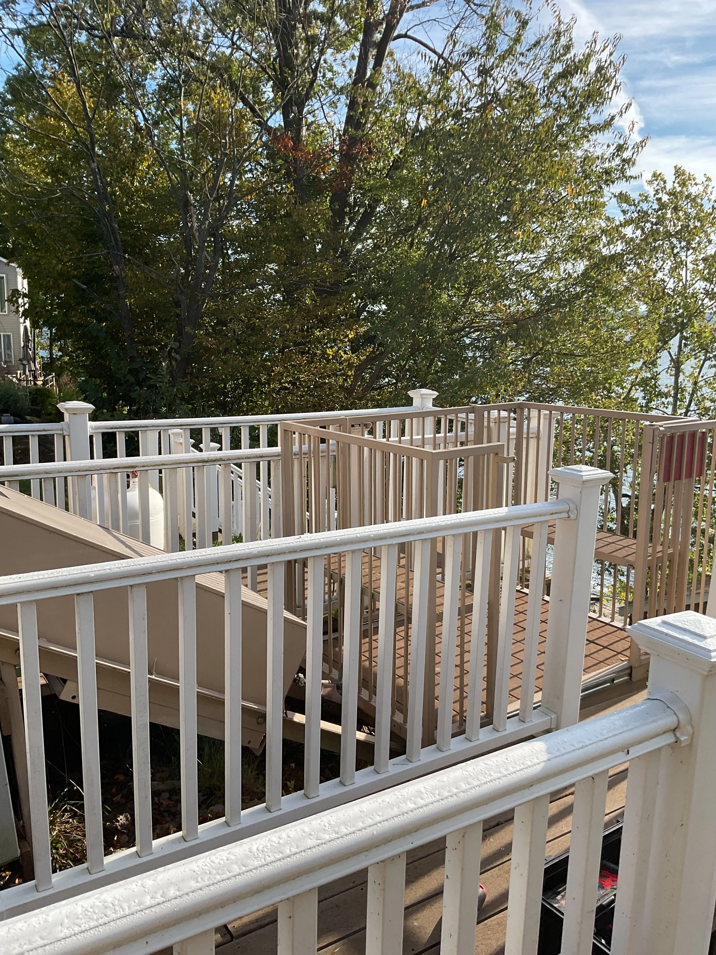 View of a backyard deck with white railing, trees and a partly cloudy sky in the background.