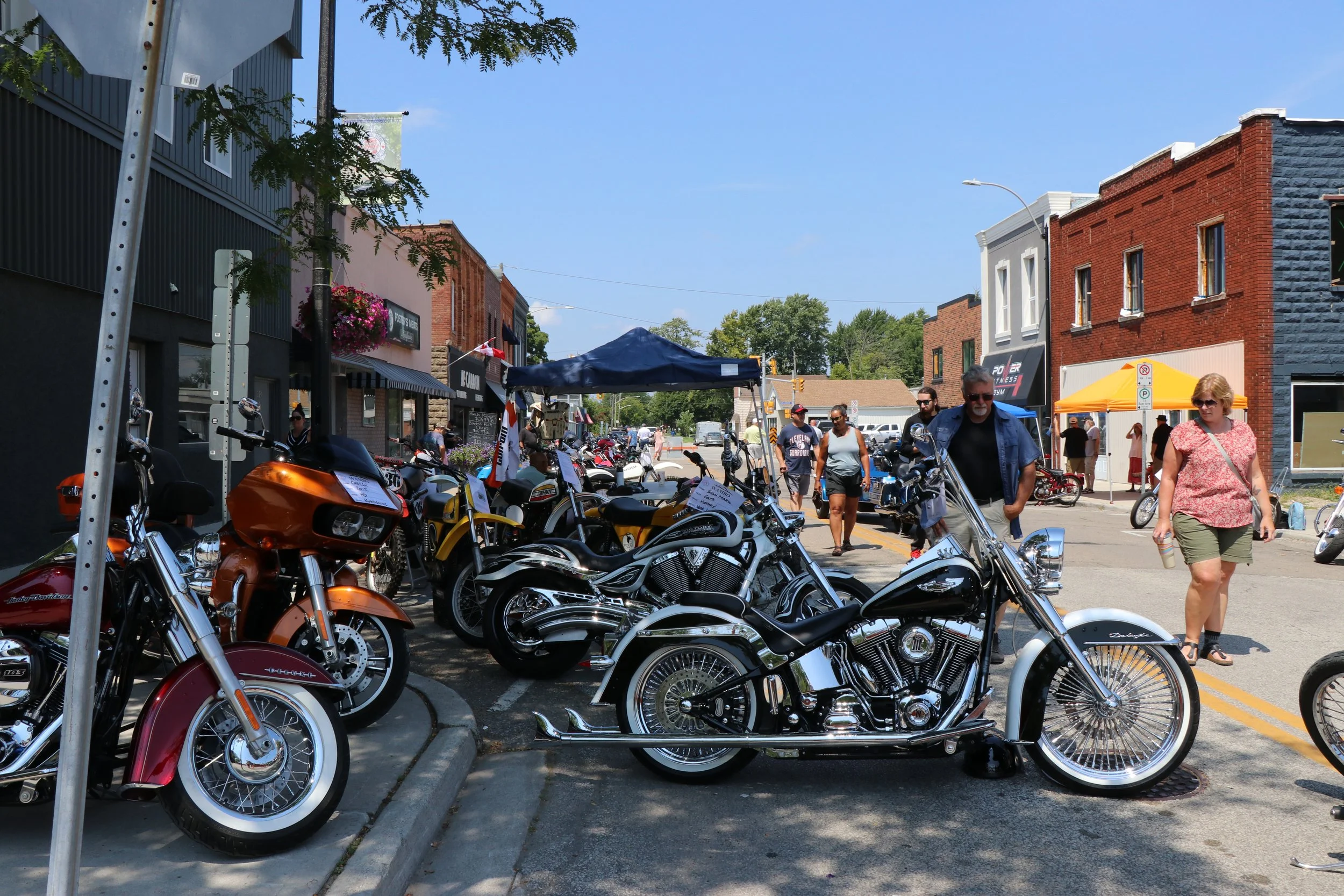 Antique motorcycles lining a downtown street in Wallaceburg with people attending WAMBO walking by and looking
