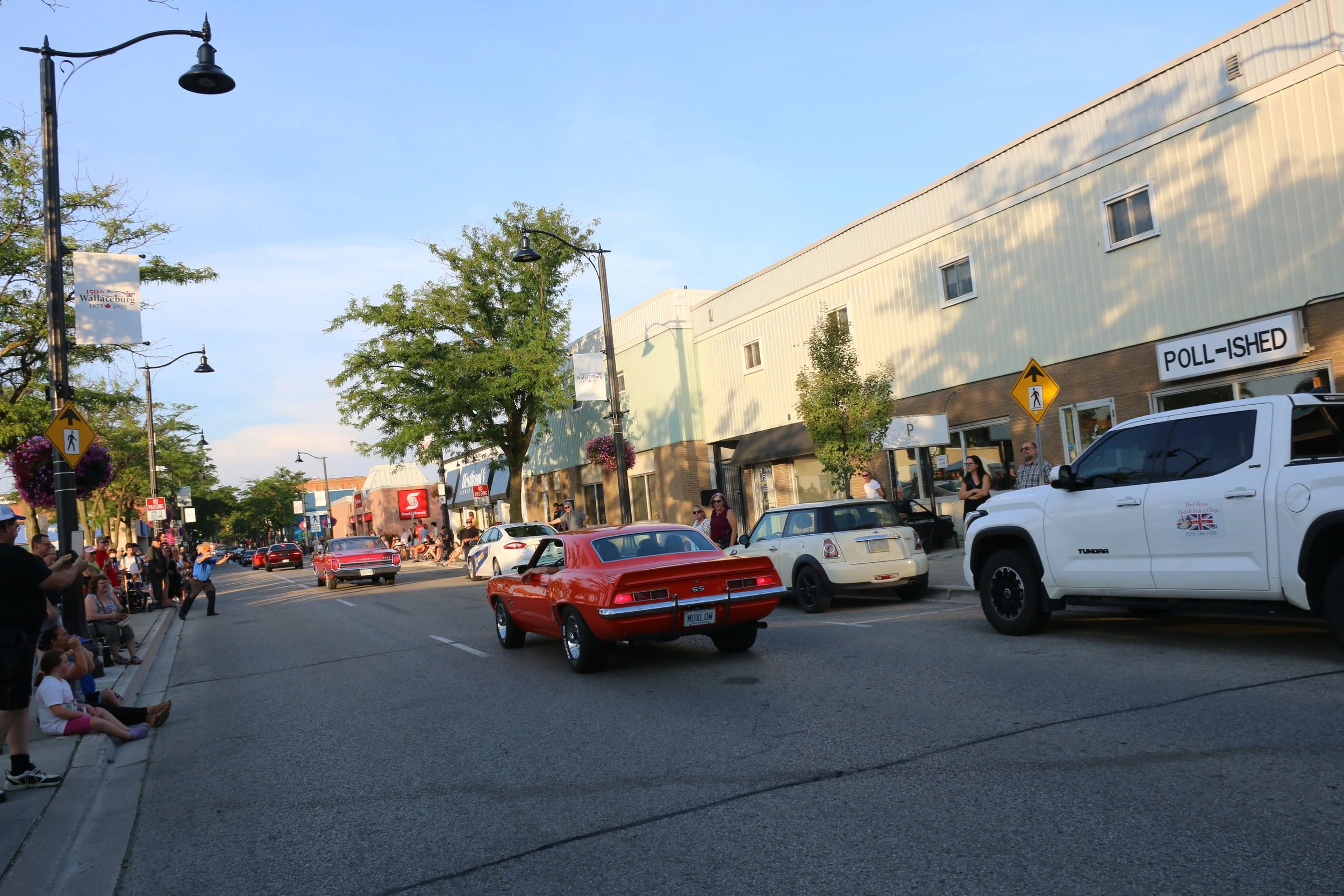Main street in downtown Wallaceburg hosting a line up of classic cars driving through a large crowd watching and cheering them on