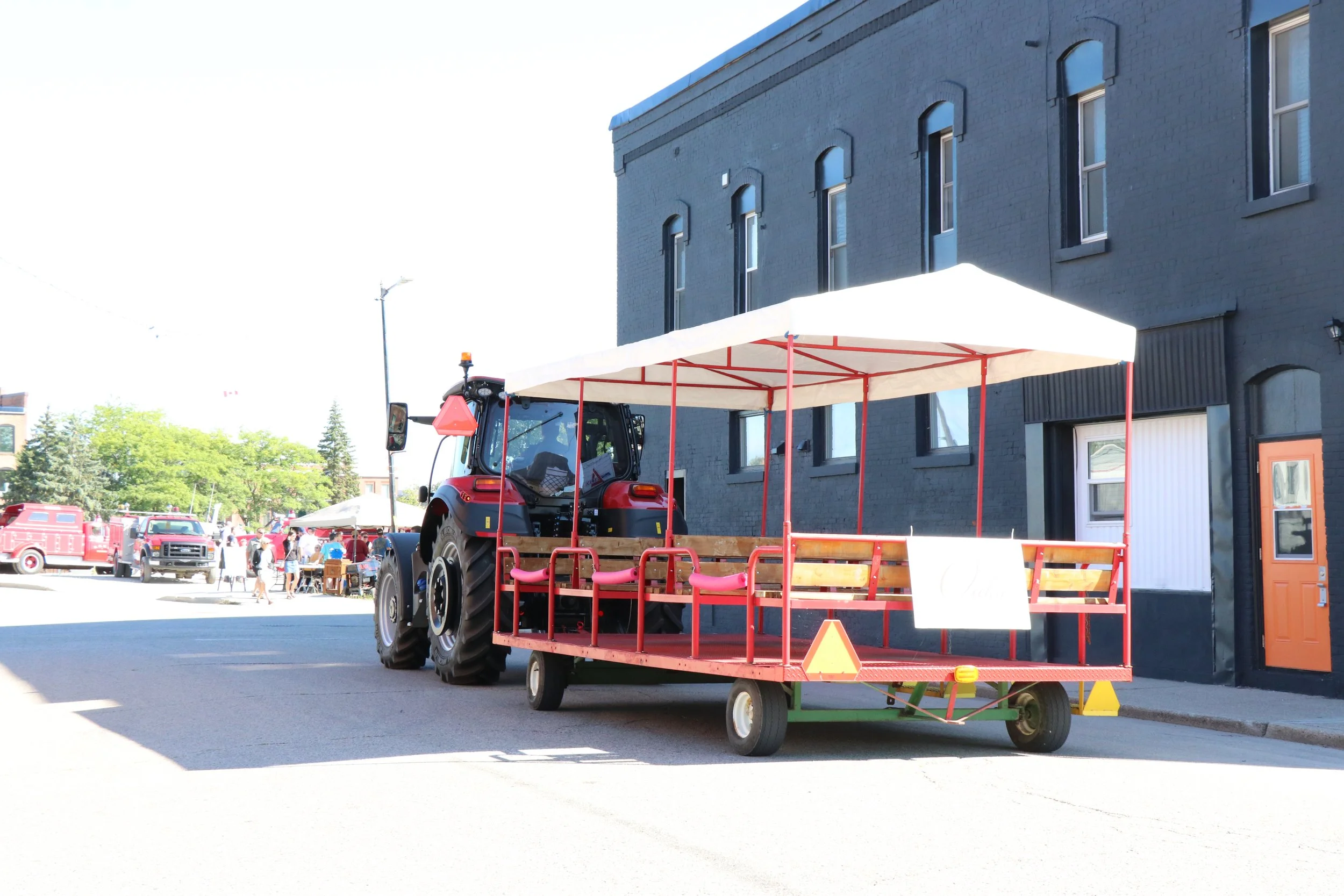 Flat bed trailer set up with a tent and benches, attached to a farming tractor to be a shuttle for people to get around to different areas of the WAMBO event