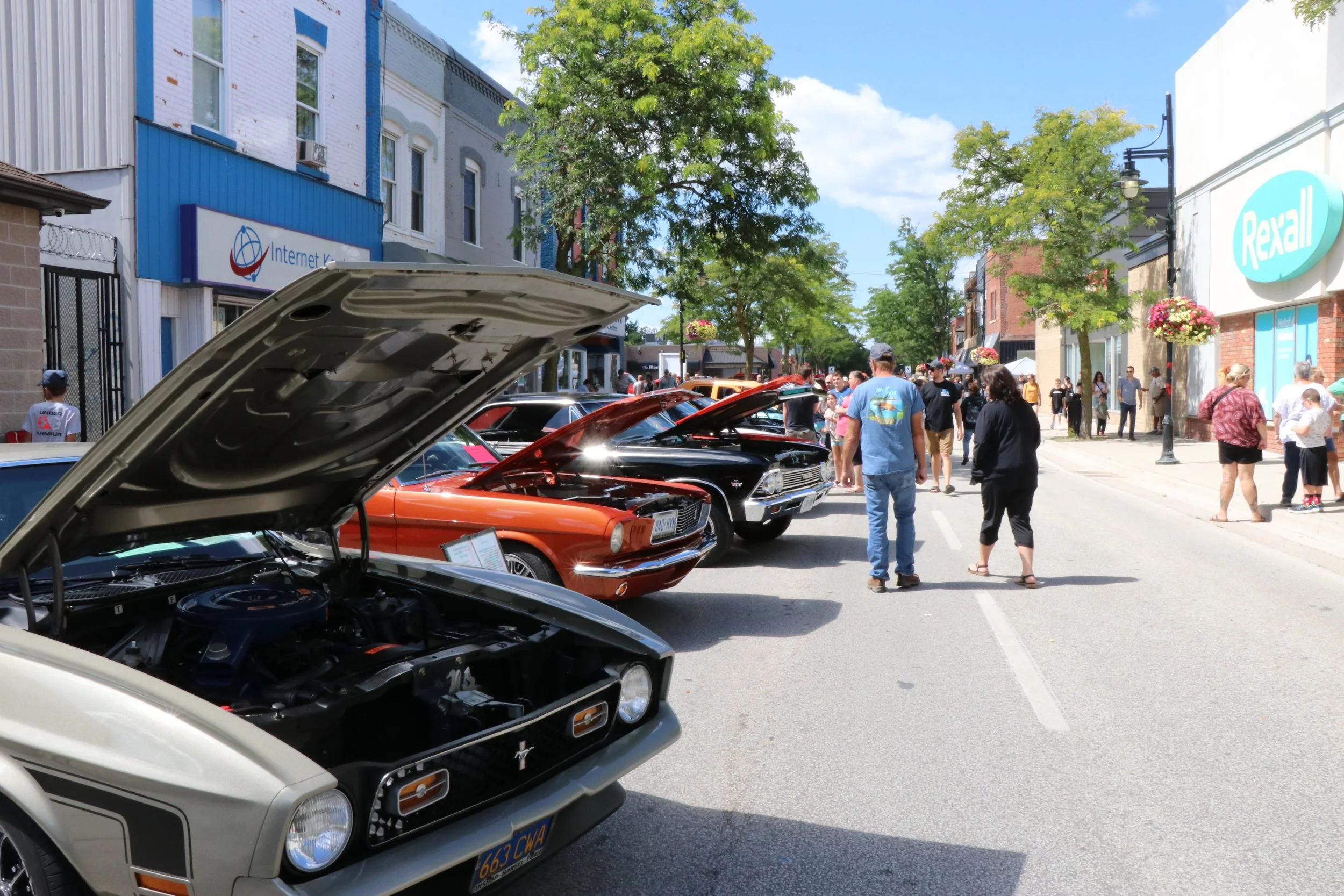 Classic and custom cars lining the downtown street of Wallaceburg surrounded by old buildings with people walking down the street looking at the cars