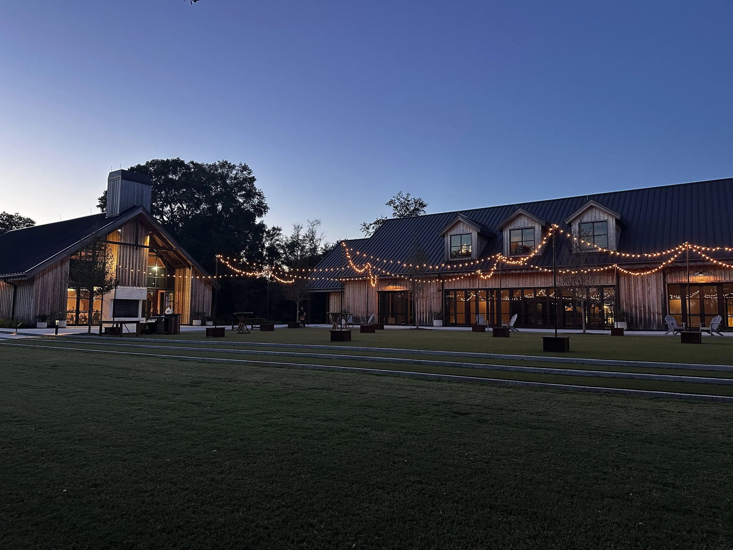 A large outdoor building complex made of wood with string lights hanging across the area during dusk or early evening.