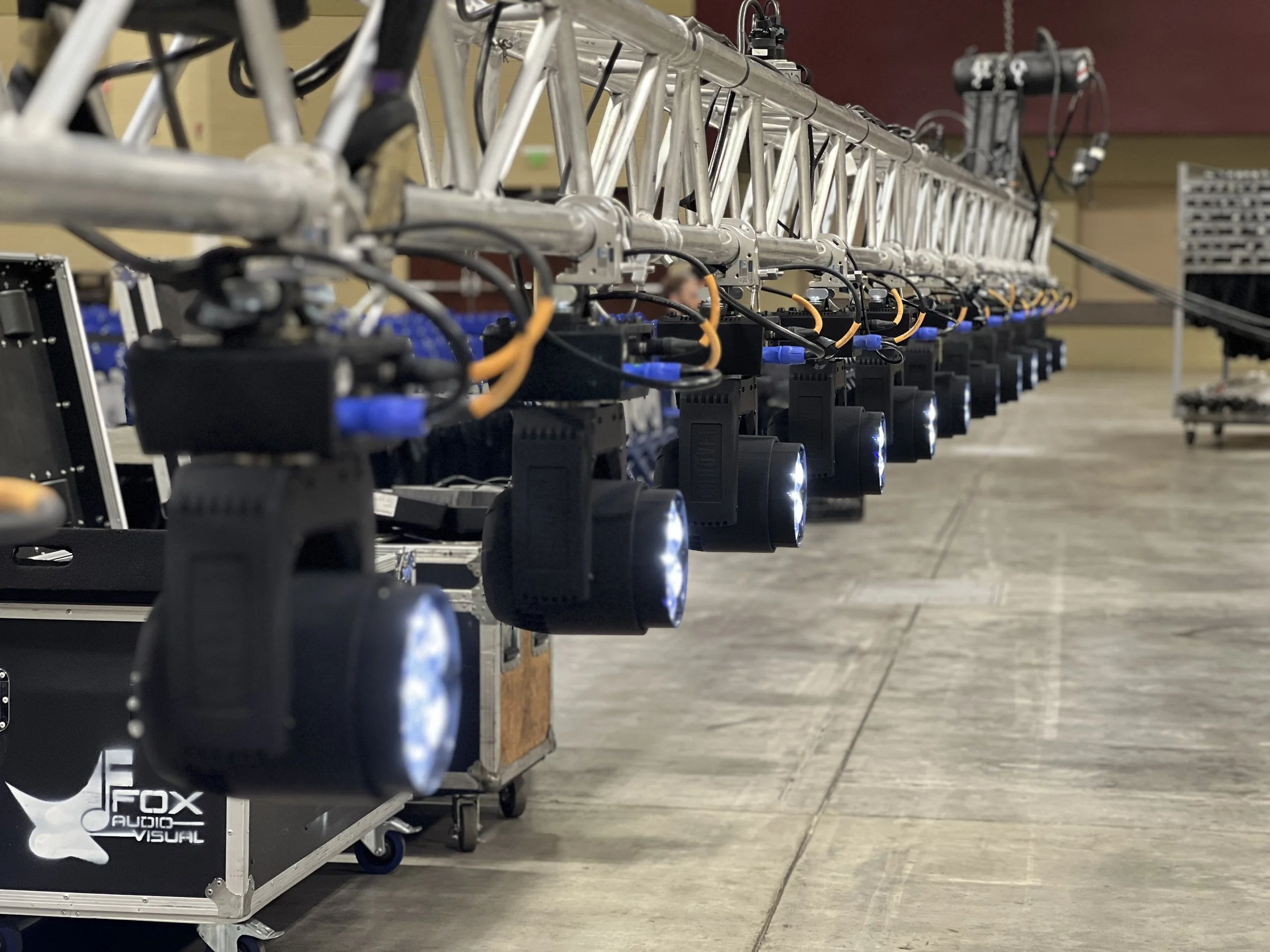 A long industrial truss with multiple mounted lights and equipment, set up in a large indoor space with concrete floors.