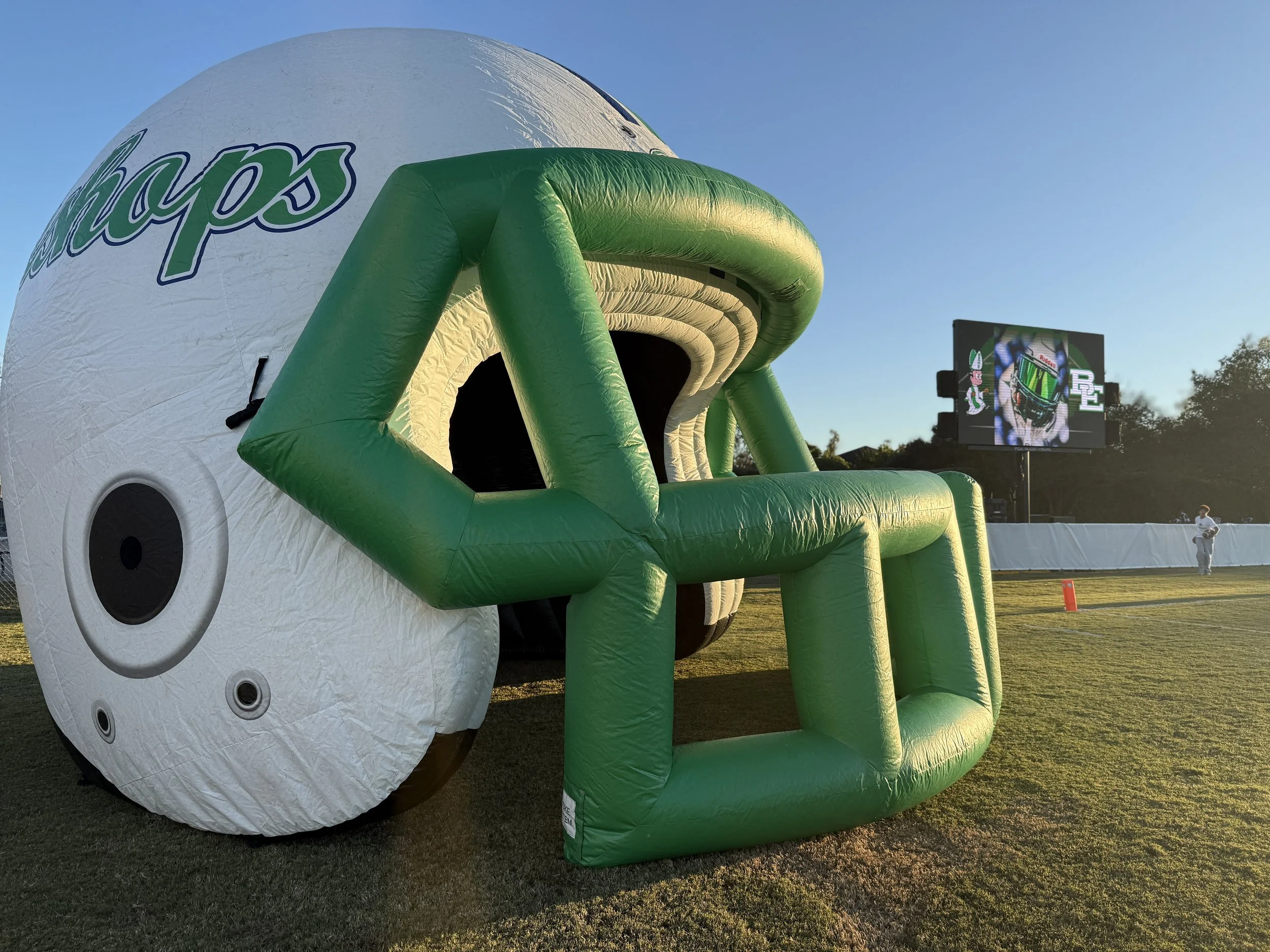 Inflatable football helmet with a green and white design on a grassy field during sunset.