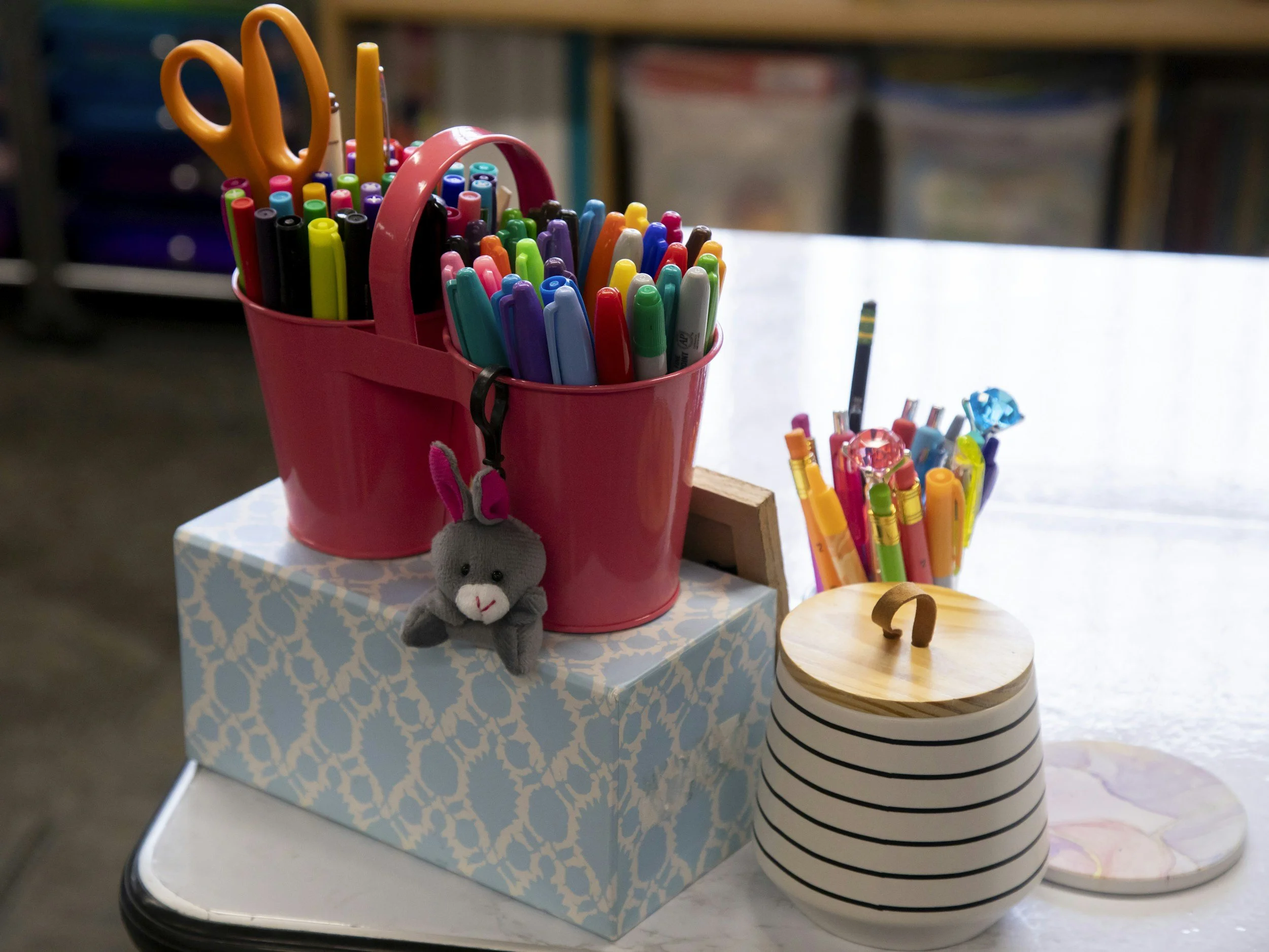 A pink container holding colorful markers and scissors on a table.