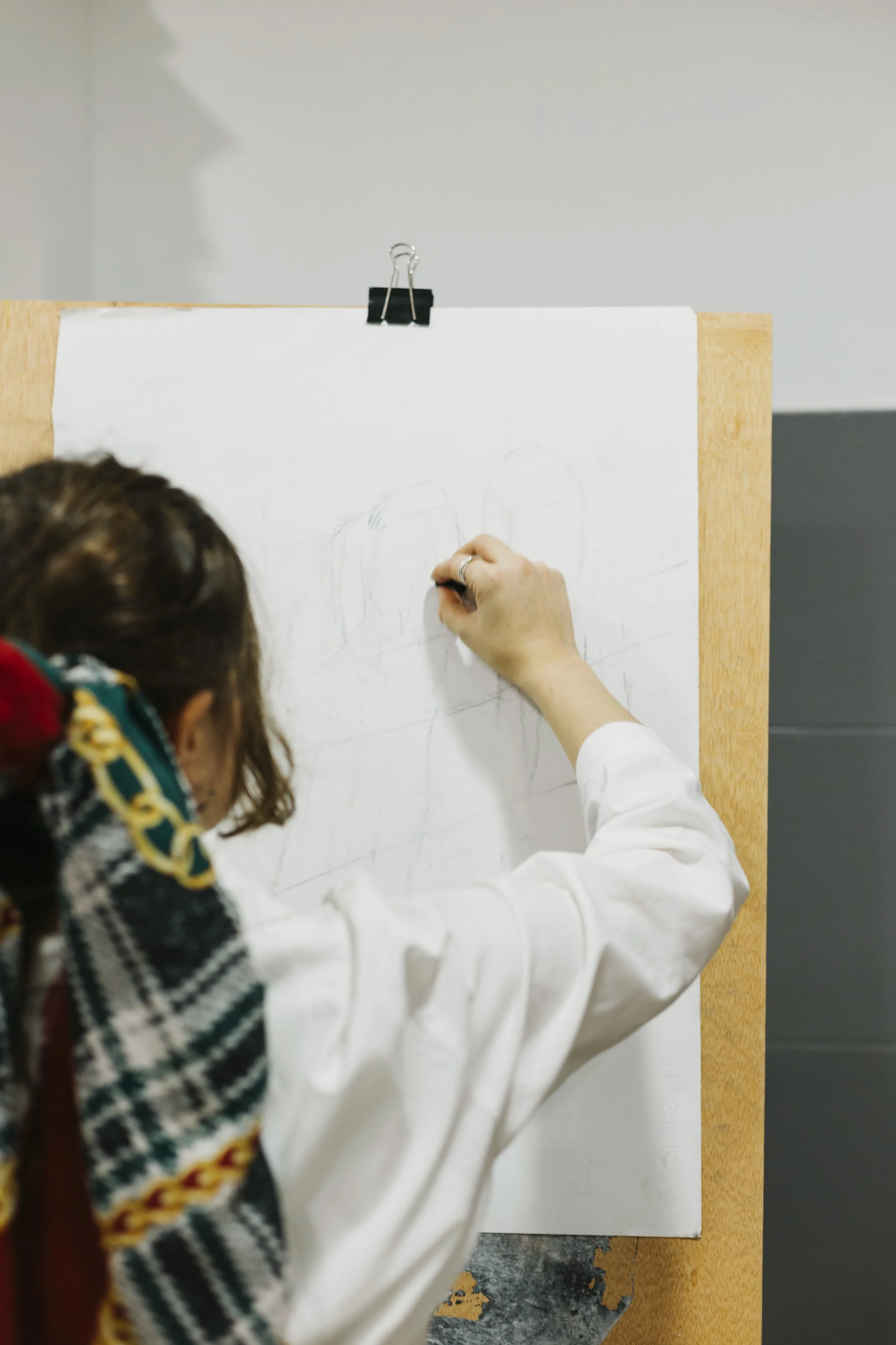 Person drawing on a white canvas clipped to a wooden board, seen from behind, with a colorful scarf on their shoulder. Free Student Art Competition open to grades 6-12. Deadline: September 1, each year. Free Entry. Middle and High School Art Contest.