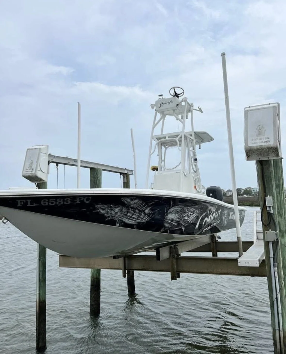 A fishing boat docked at a pier with a water view, featuring a black hull with fish illustrations, a white center console, and various antennas and poles.