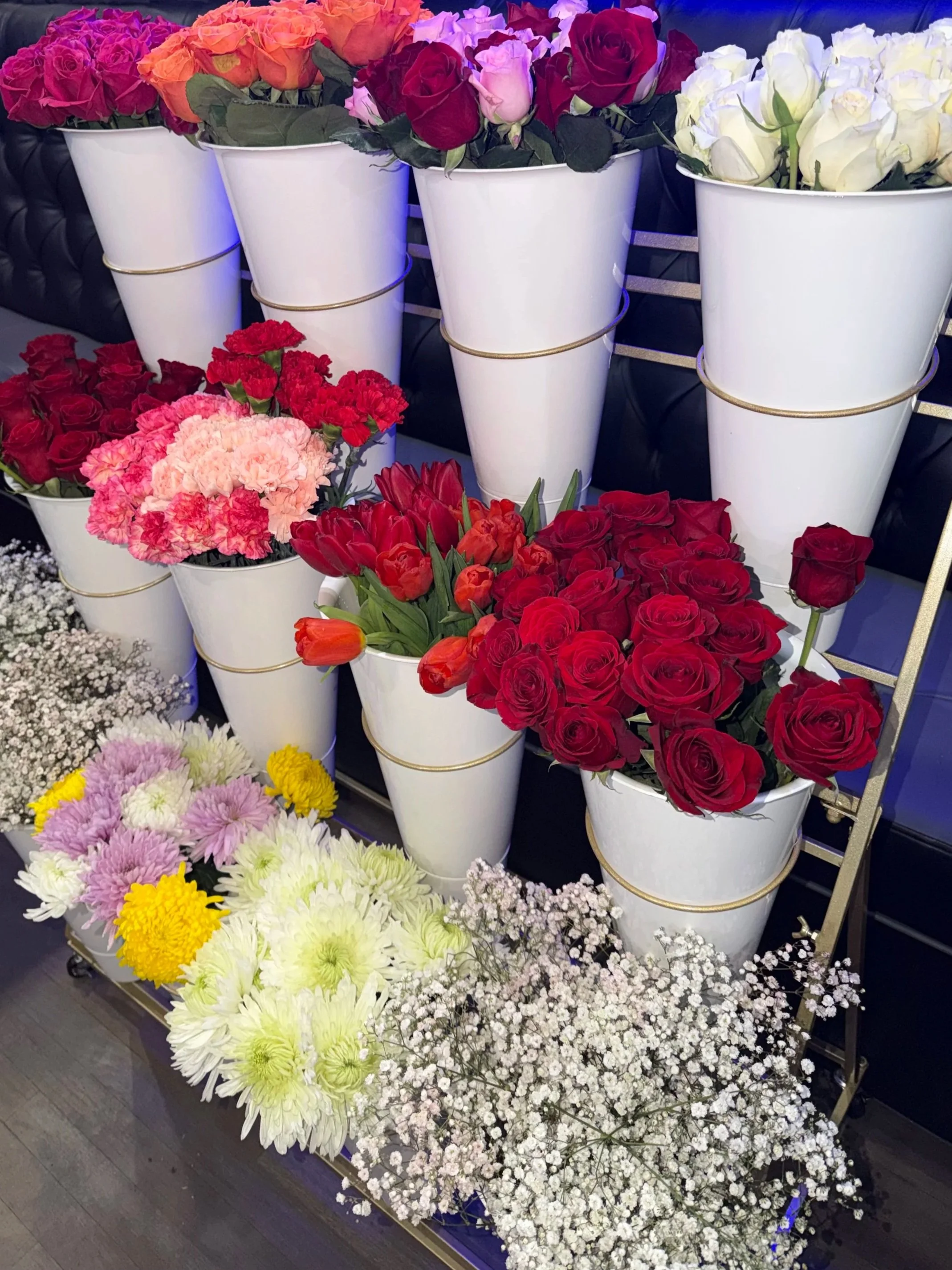 Various colorful flower bouquets, mainly roses, displayed in white buckets on a metal cart.