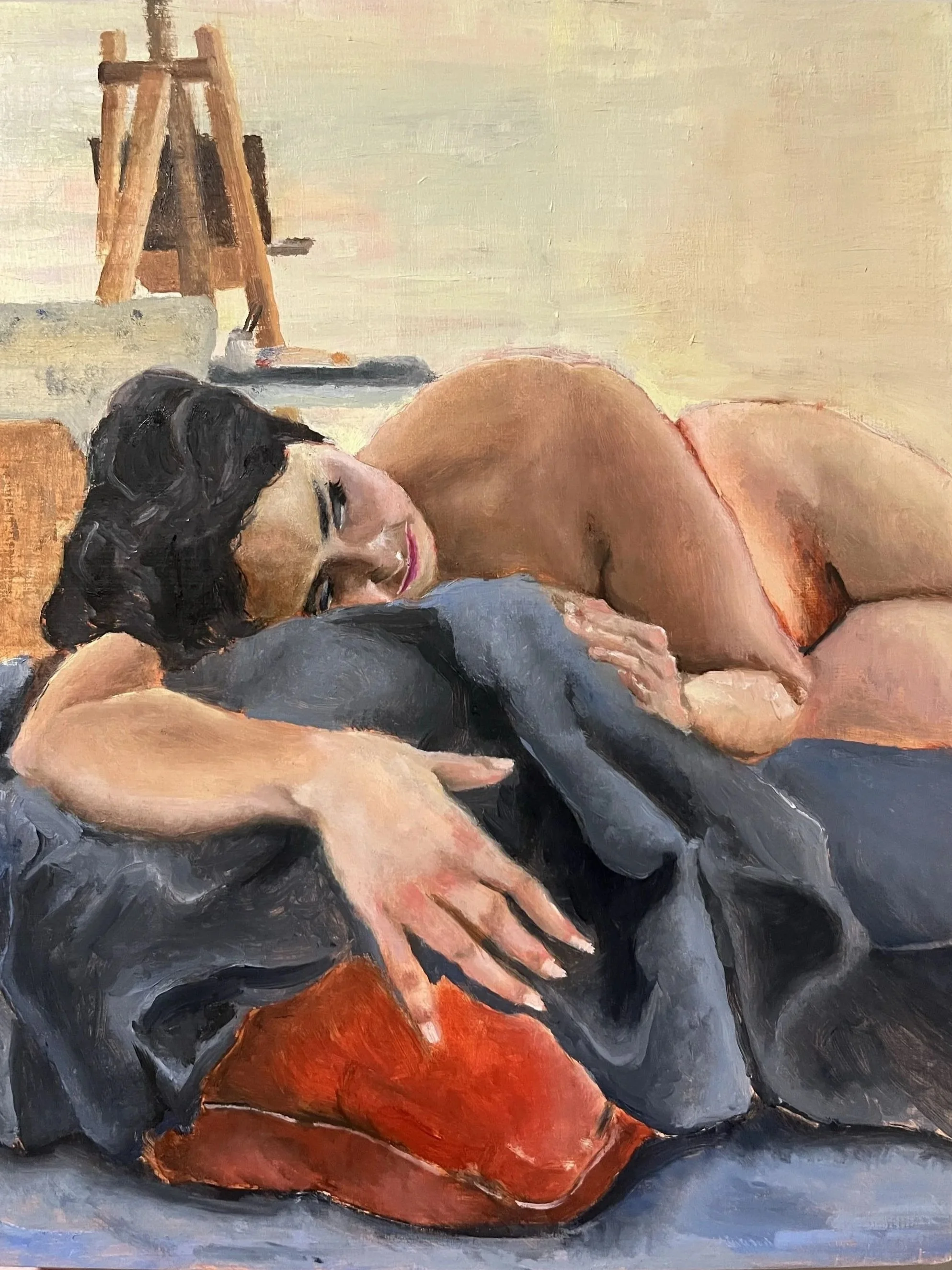 A woman lying on a bed with her eyes half-open, dark hair, and a neutral expression. The background includes an artist's easel and supplies.
