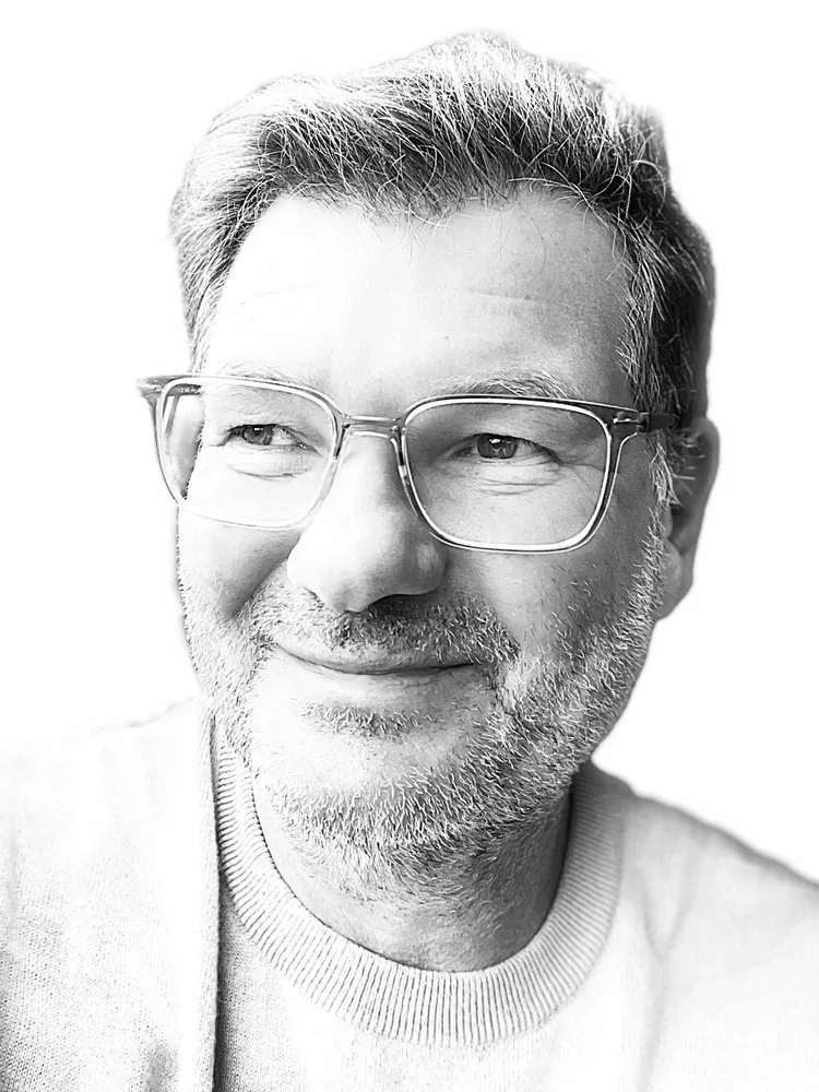 Schwarz-weiß Porträt von Ernst Brandt mit Brille, grauem Haar und Bart, lächelnd, in einem hellen Hemd.