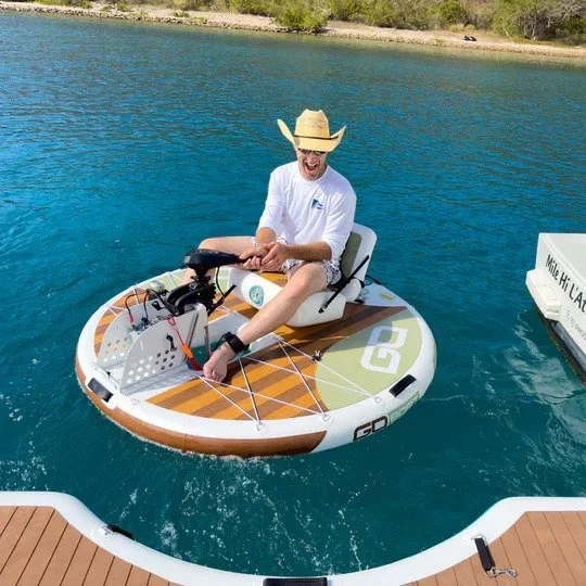 Person in a white shirt and straw hat riding an electric paddleboard on a lake.