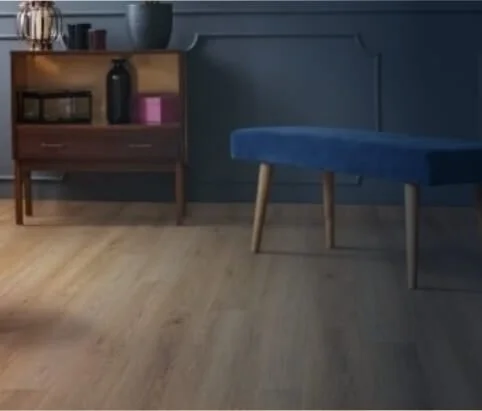 A wooden side table with books and decorative items, and a blue upholstered bench with wooden legs against a dark blue wall and wood flooring.
