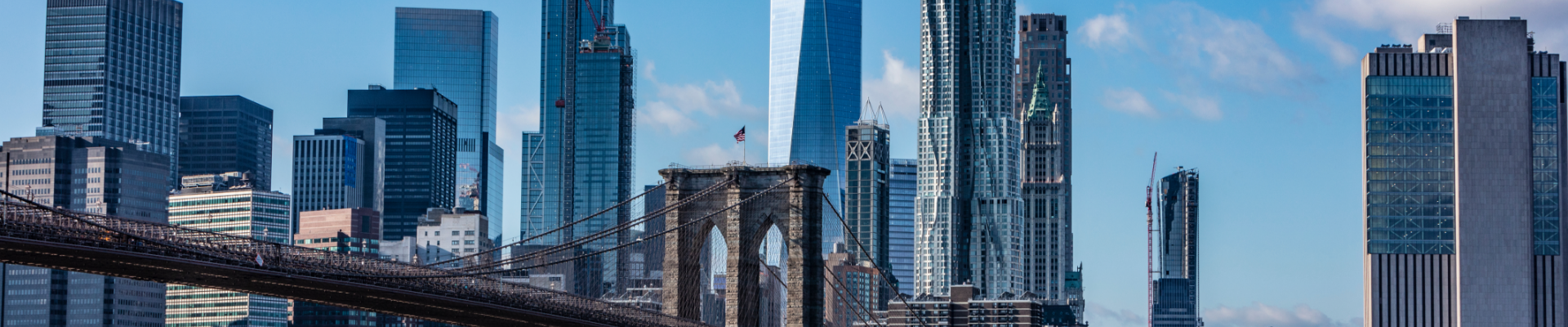 Skyline view of Manhattan, New York City, featuring the Brooklyn Bridge in the foreground and various skyscrapers including One World Trade Center in the background.