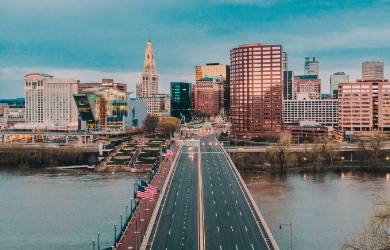 A city skyline with a bridge over a river, featuring various tall buildings and a clear sky.