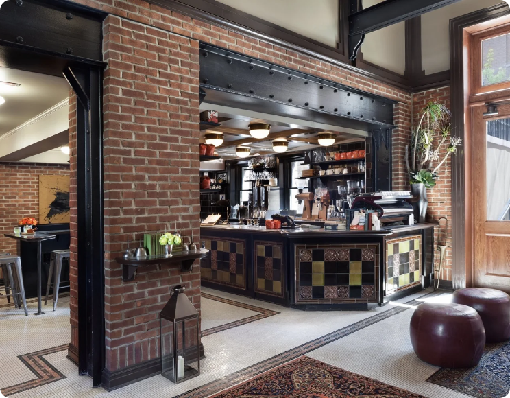Interior of a cozy restaurant with a brick wall, a counter with colorful tiles, and a potted plant near a large window