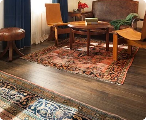 Living room with a wooden coffee table, a brown upholstered sofa, a yellow armchair, a small side table with a red flower arrangement, and decorative area rugs on a dark hardwood floor.