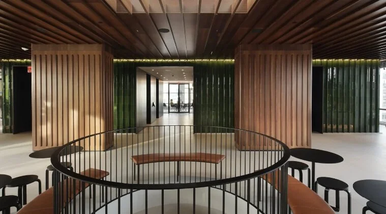Modern interior space with wooden and green wall panels, a curved seating area with black railings, and small round black tables and stools.