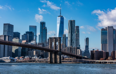 View of the New York City skyline with the Brooklyn Bridge crossing the water in the foreground.