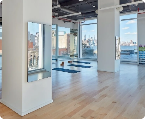 Sunlit yoga studio with large windows, workout mats, and a city skyline view.