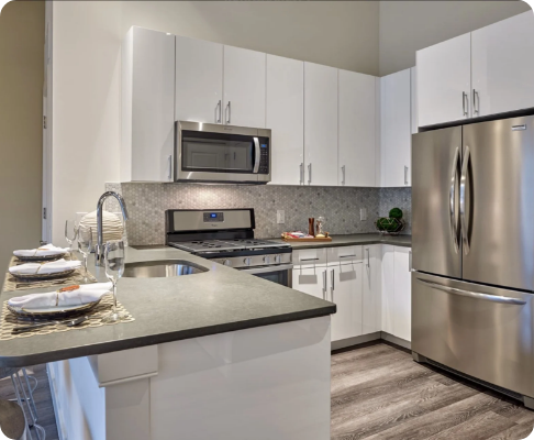 Modern kitchen with white cabinets, stainless steel appliances including a refrigerator, microwave, and oven, granite countertops, a sink, and a small breakfast bar with plates and silverware.