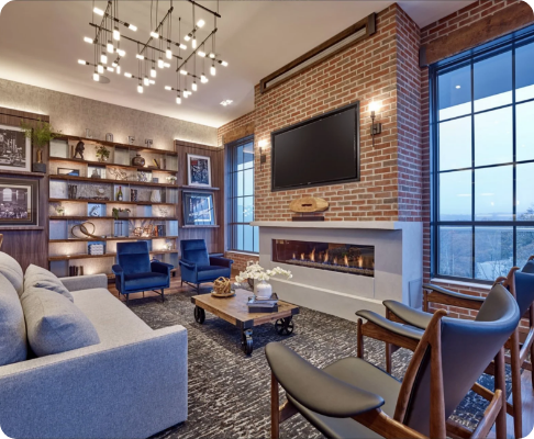 Modern living room with brick accent wall, wall-mounted TV, fireplace, large windows, and contemporary furniture including a sofa, armchairs, and a coffee table.