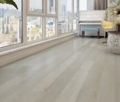 Empty room with large windows, hardwood floor, and a few pieces of furniture in the corner.