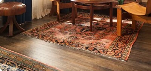A wooden table with a rounded edge and a smaller rectangular table in a room with hardwood flooring and patterned area rugs.