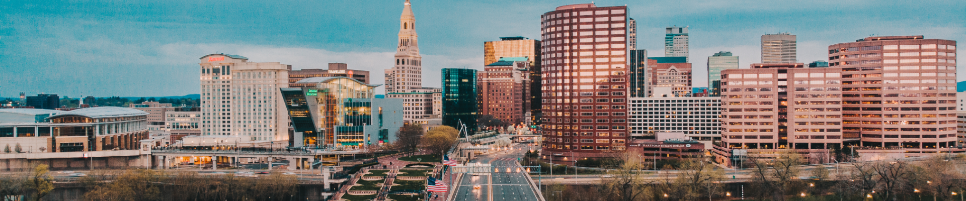 A city skyline at dusk with high-rise buildings, roads, and a central tower