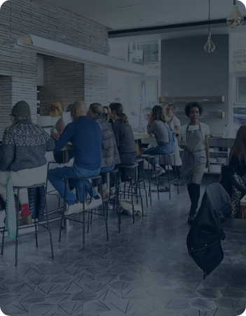 People sitting on barstools at a counter in a modern cafe with white brick walls and hanging light fixtures.