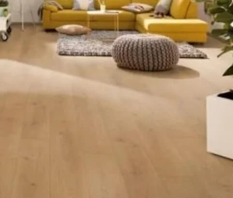 A cozy living room with a yellow couch, a gray textured pouf, a small round pillow, a gray rug, and a wooden floor.