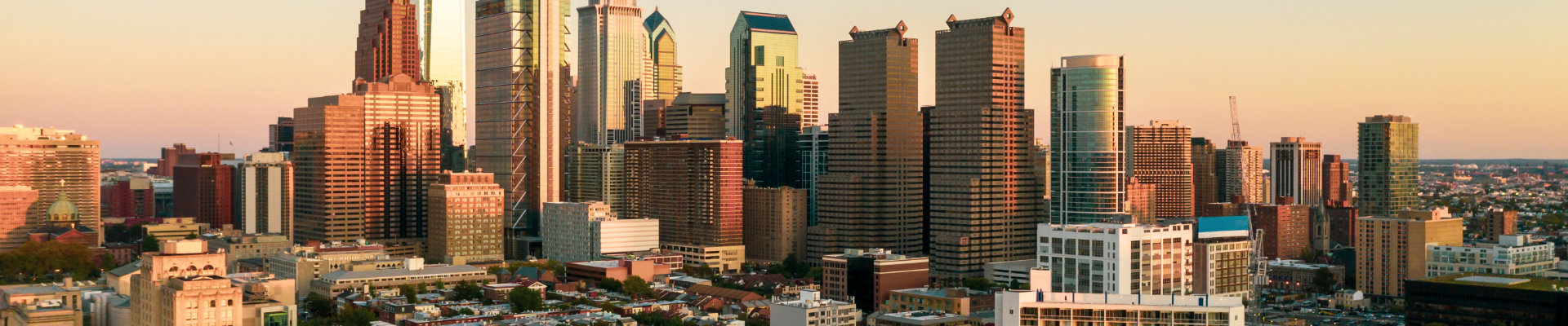 Sunset view of downtown skyscrapers in a city skyline, with tall modern buildings and shorter historic structures in the foreground.