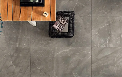 Gray tiled floor with a black wire basket and a wooden table with a small white block and a magazine on top.