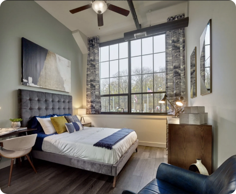 Modern bedroom with large window, tufted gray bed, and minimal decor.