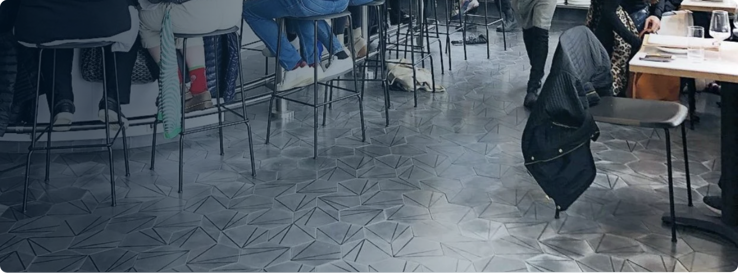 People sitting and standing at tables in a restaurant or cafe with patterned tile floor.