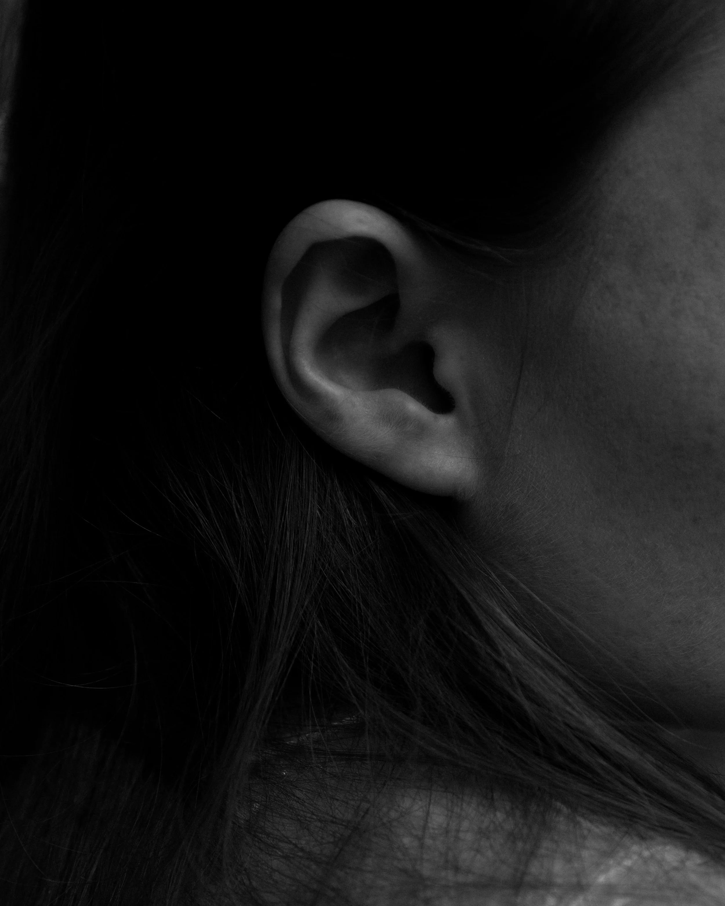 Close-up black and white photo of a human ear with surrounding hair.