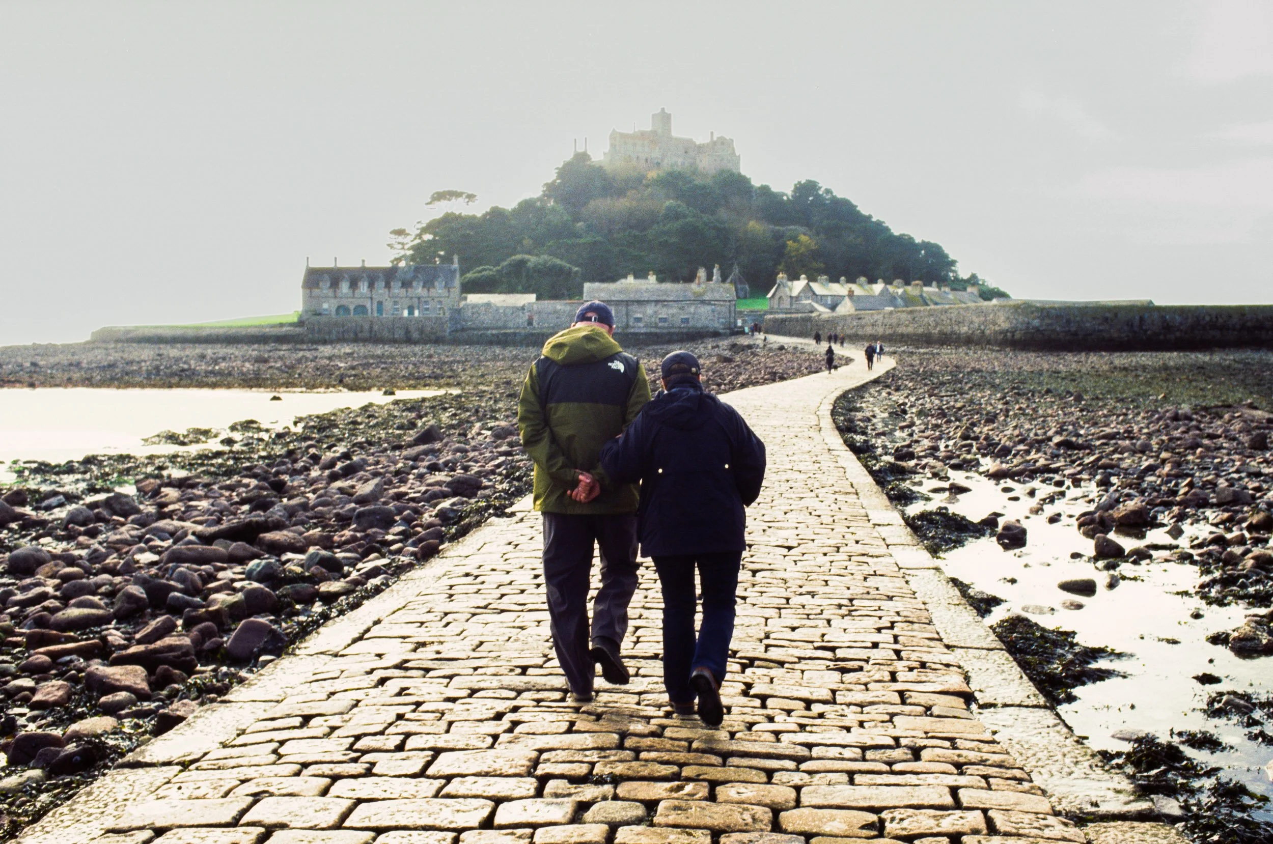 A couple hold hands walking the causeway to St Michael's Mount