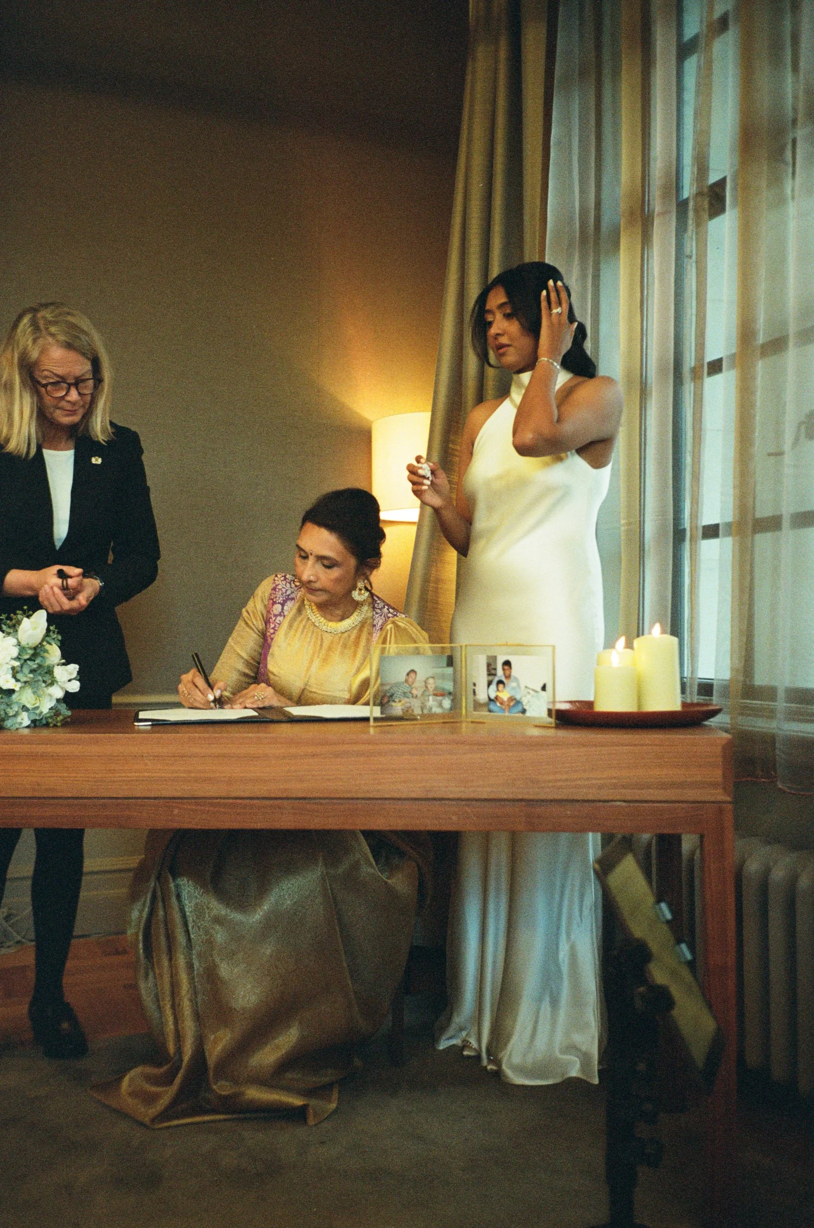 Mother signing the wedding register while the bride watches from the window