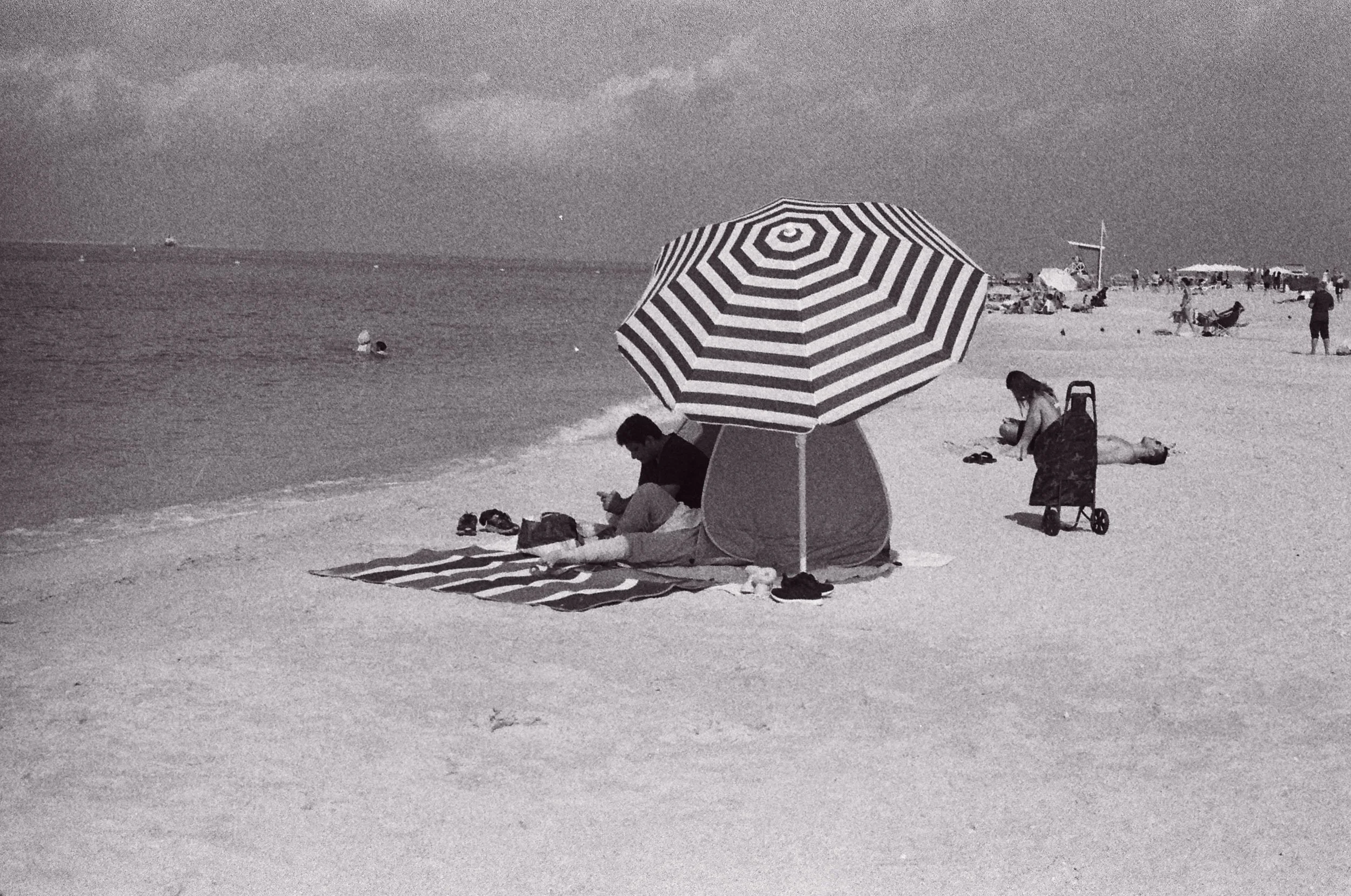 Striped umbrella, beach trolley and a sunbather lying flat on the sand